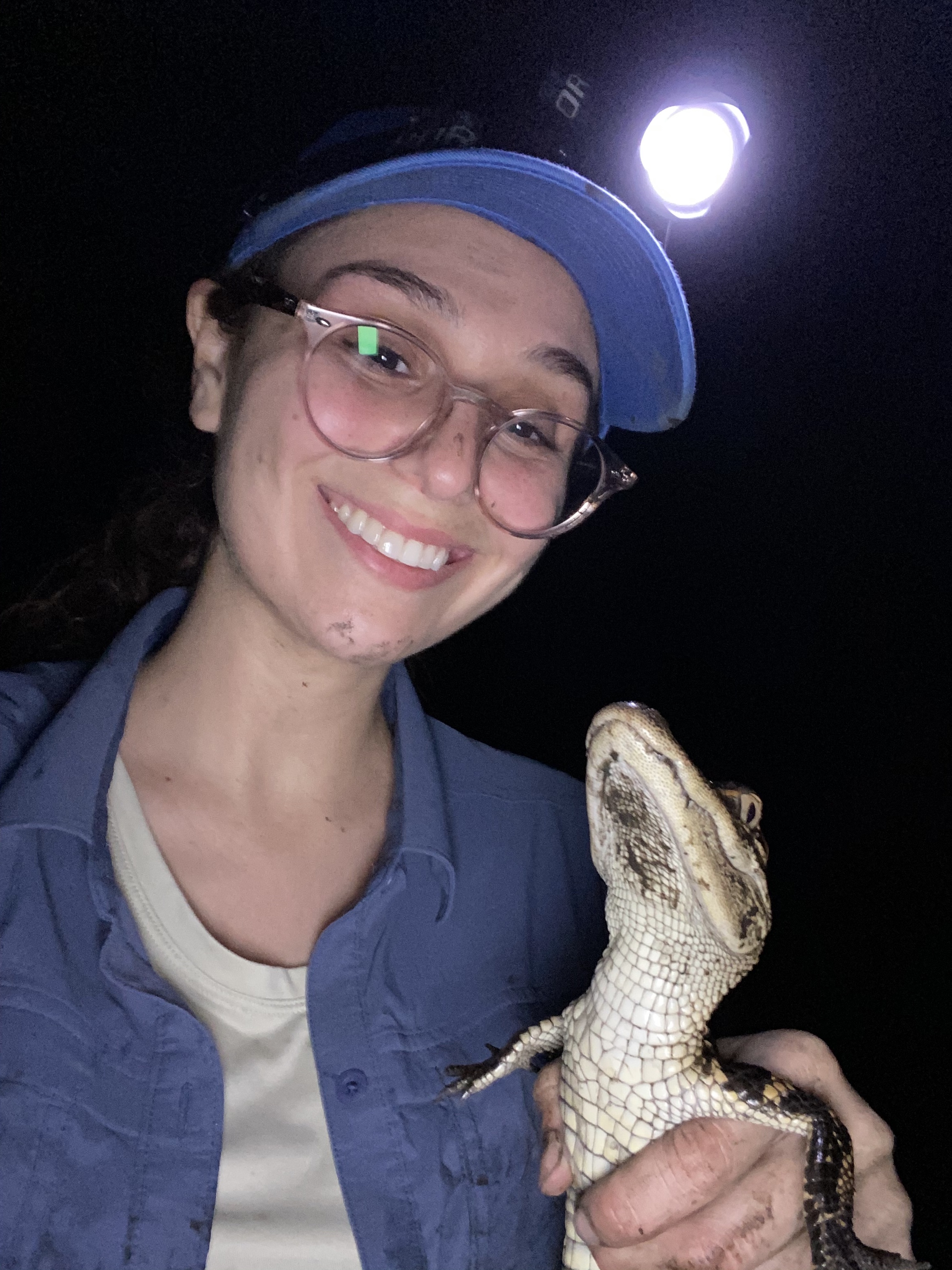 Scientist holds her subject, a baby alligator, and smiles at the camera.